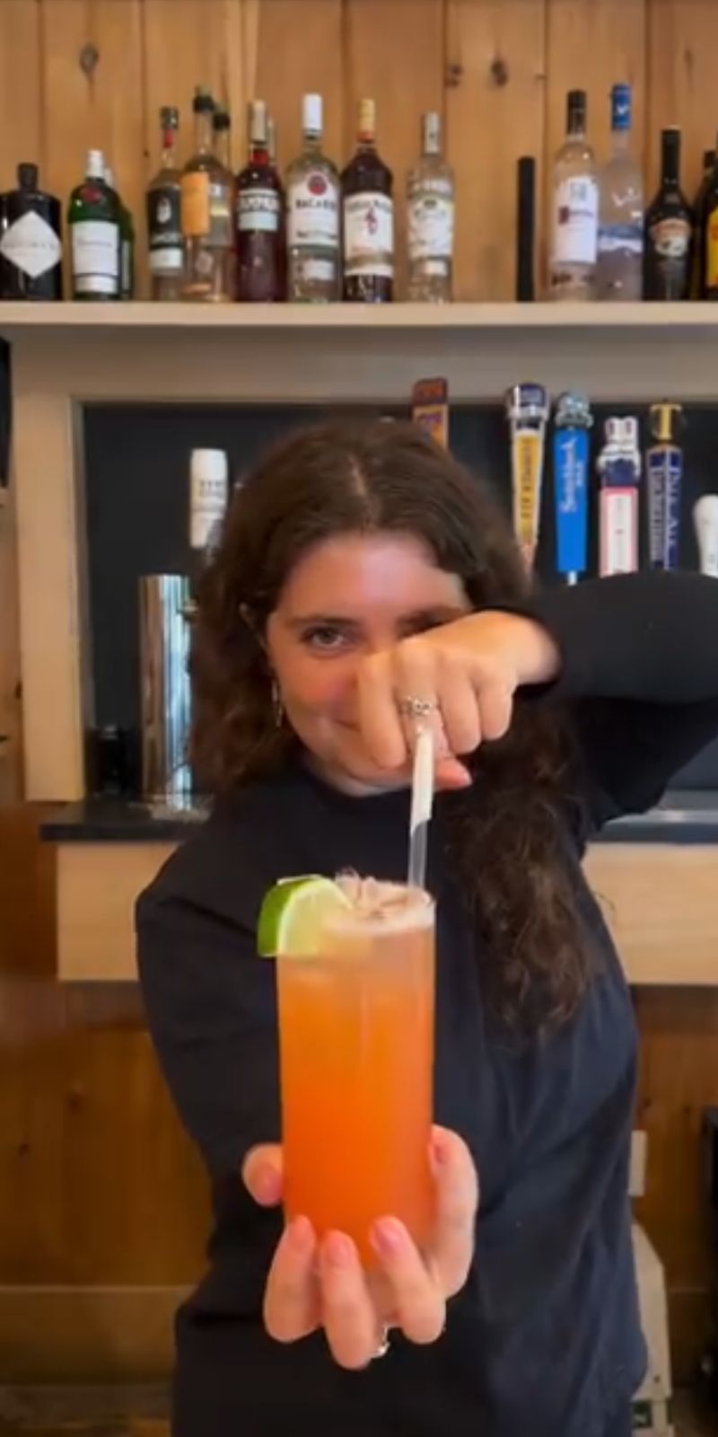 A bartender holding out a cocktail garnished with lime