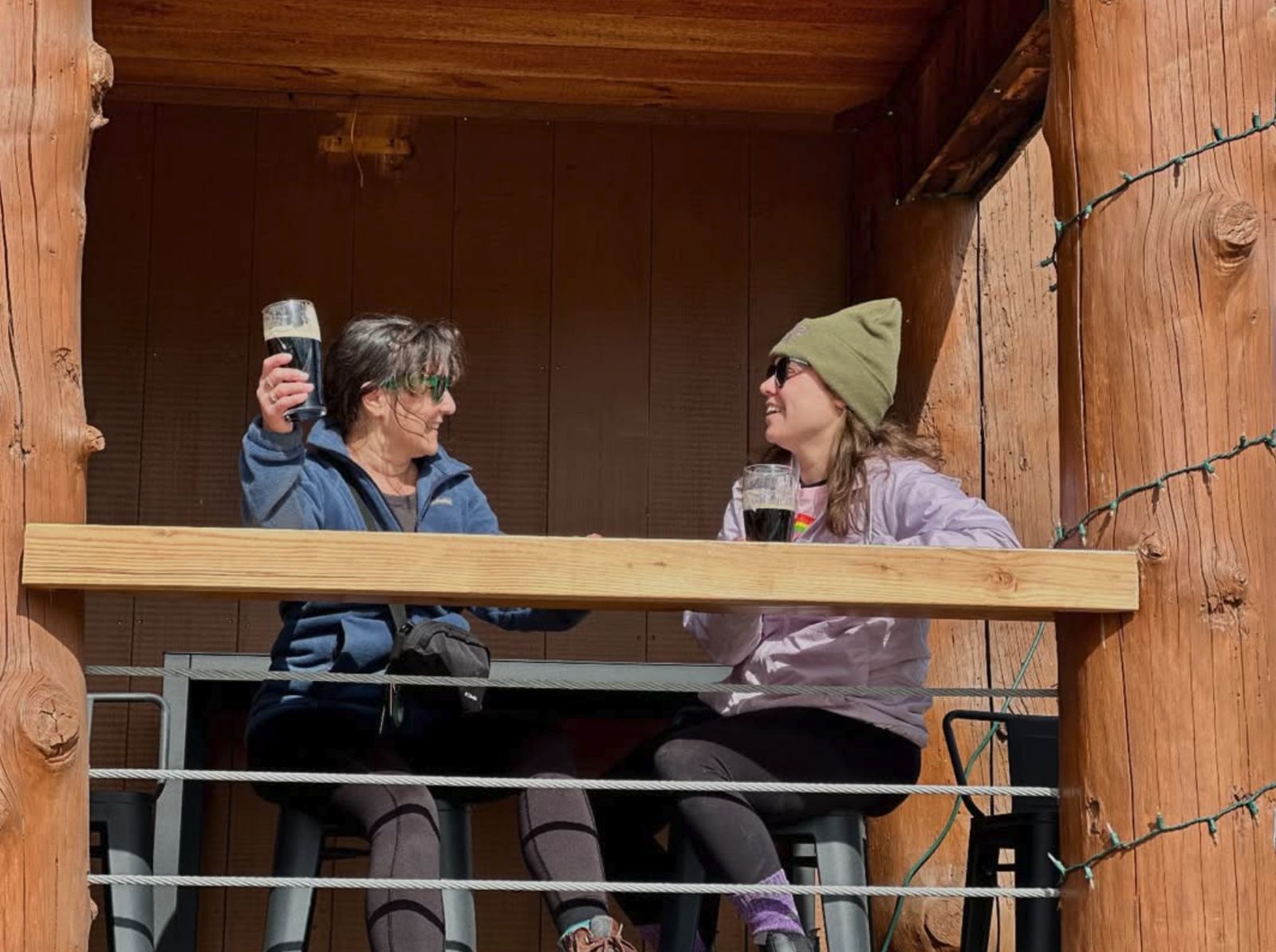 Two friends raising pints of stout at a table on Alpine Pizza's deck