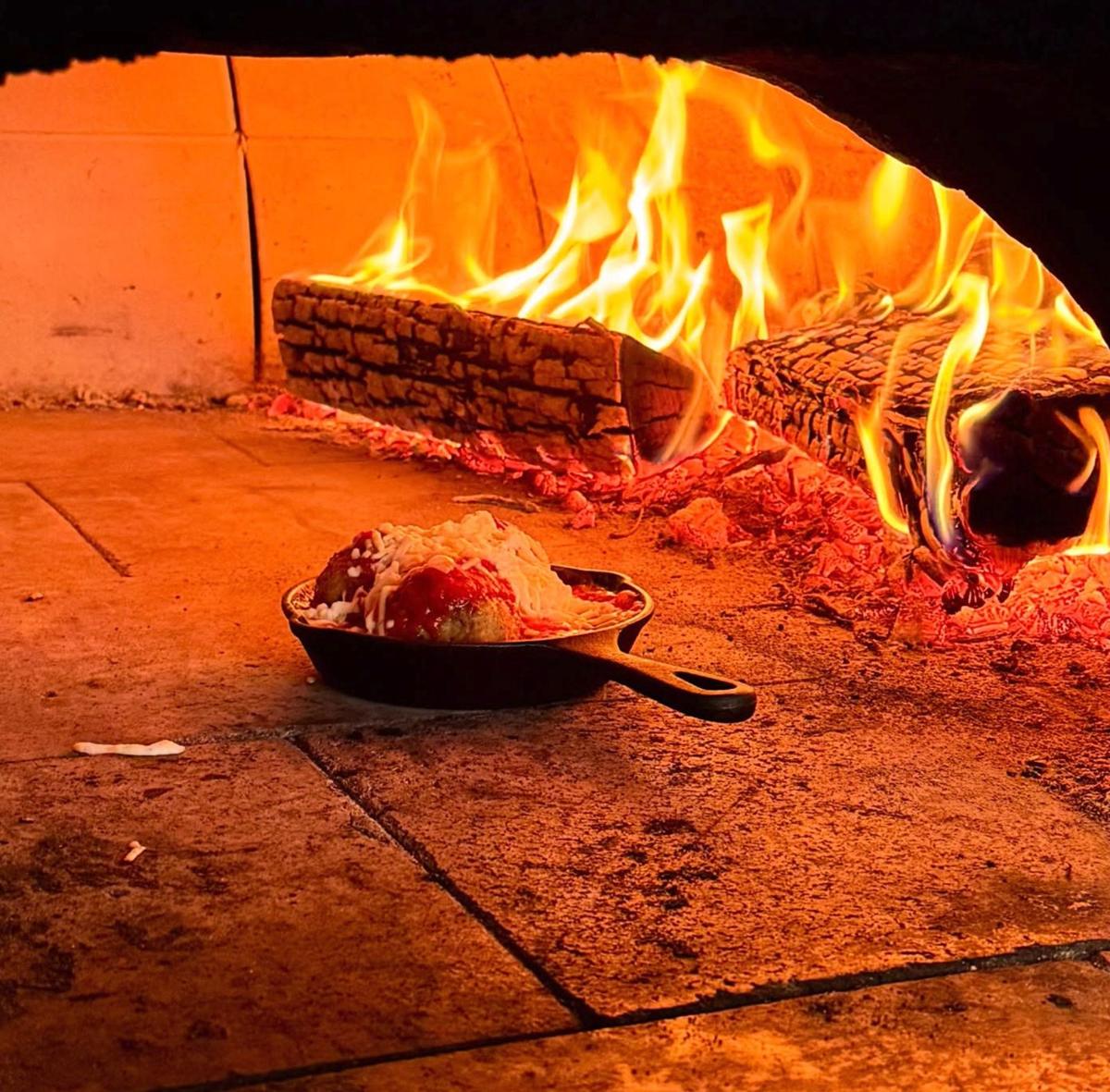 Wood-oven meatballs in a cast-iron skillet next to the fire