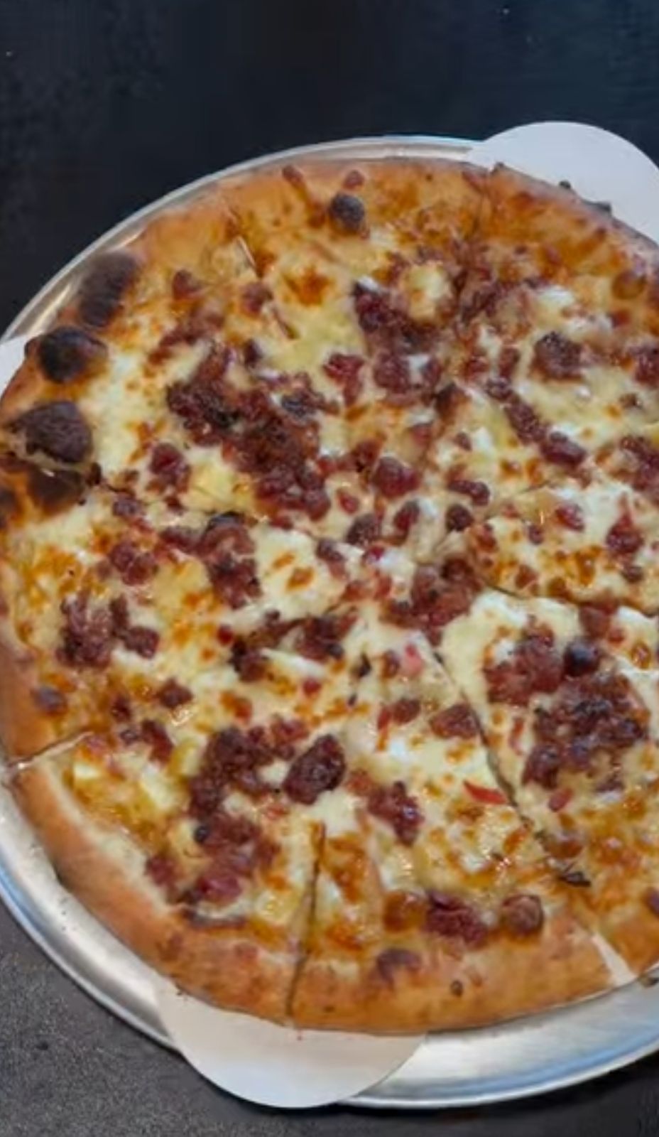 A wood-fired pizza with bacon and melted cheese, sliced on a tray